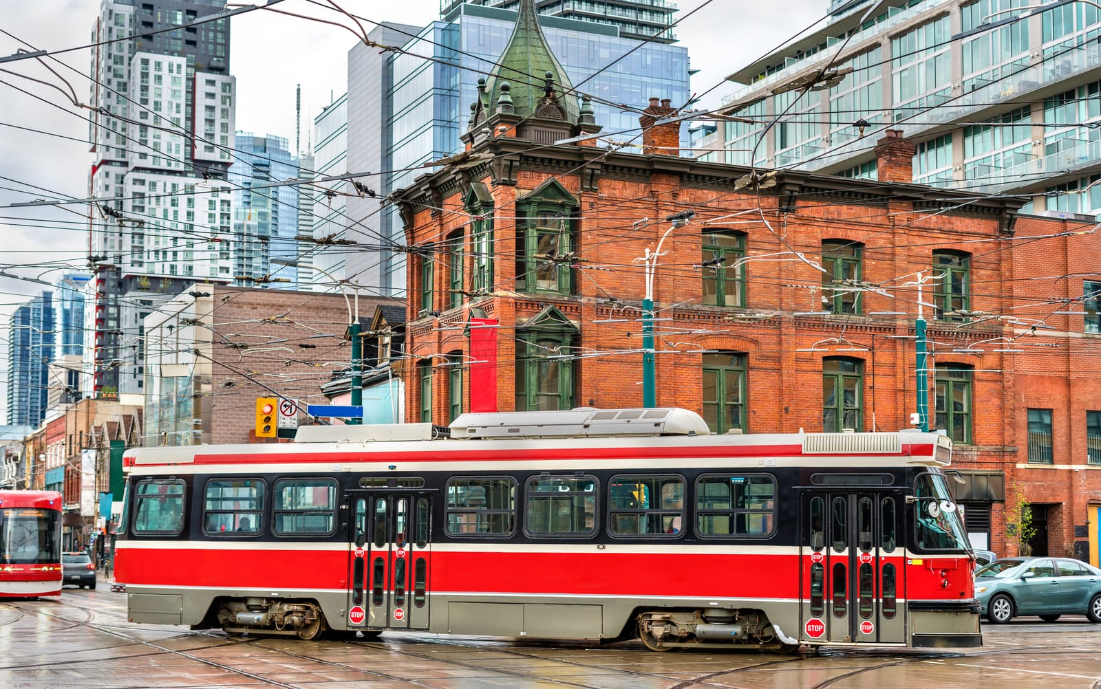 A red-and-white streetcar passing a Victorian red-brick building at Queen Street West and Spadina Avenue